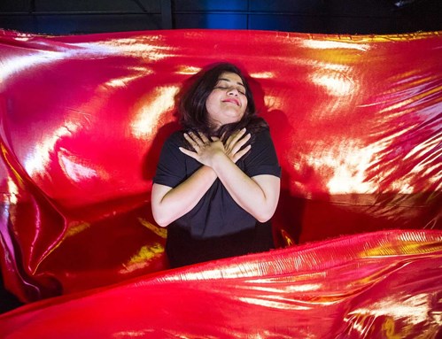Parveen lays down in what's been made to look like a bed amongst red fabric 