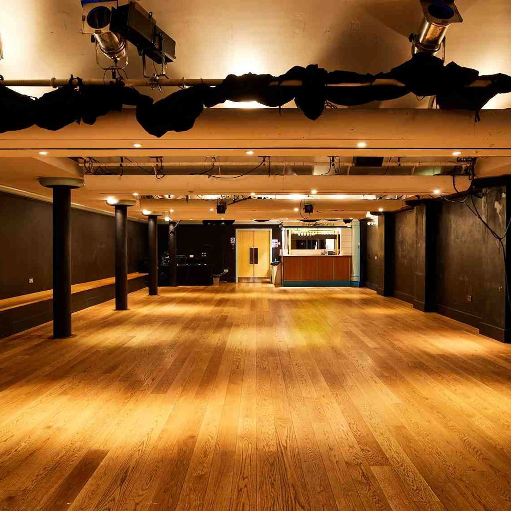 The Lawrence Batley theatre's Cellar Theatre. A large space with wooden floors and painted black walls with a lighting rig on the ceiling. 