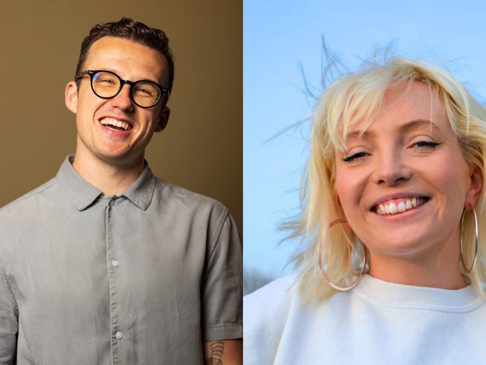 Side-by-side portraits of two smiling comedians. On the left, a man with short dark hair, wearing glasses and a light grey button-up shirt, stands against a plain tan background. On the right, a woman with platinum blonde hair and fringe, wearing hoop earrings and a fluffy white top, poses with her chin resting on her fists, smiling in front of a dark background with purple lighting.