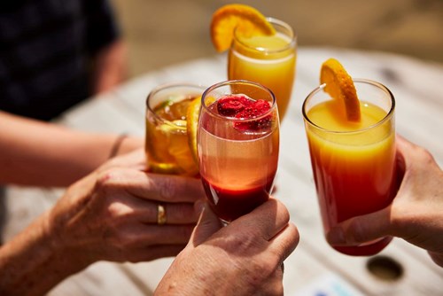 Four different cocktails in glasses are held closely together. 