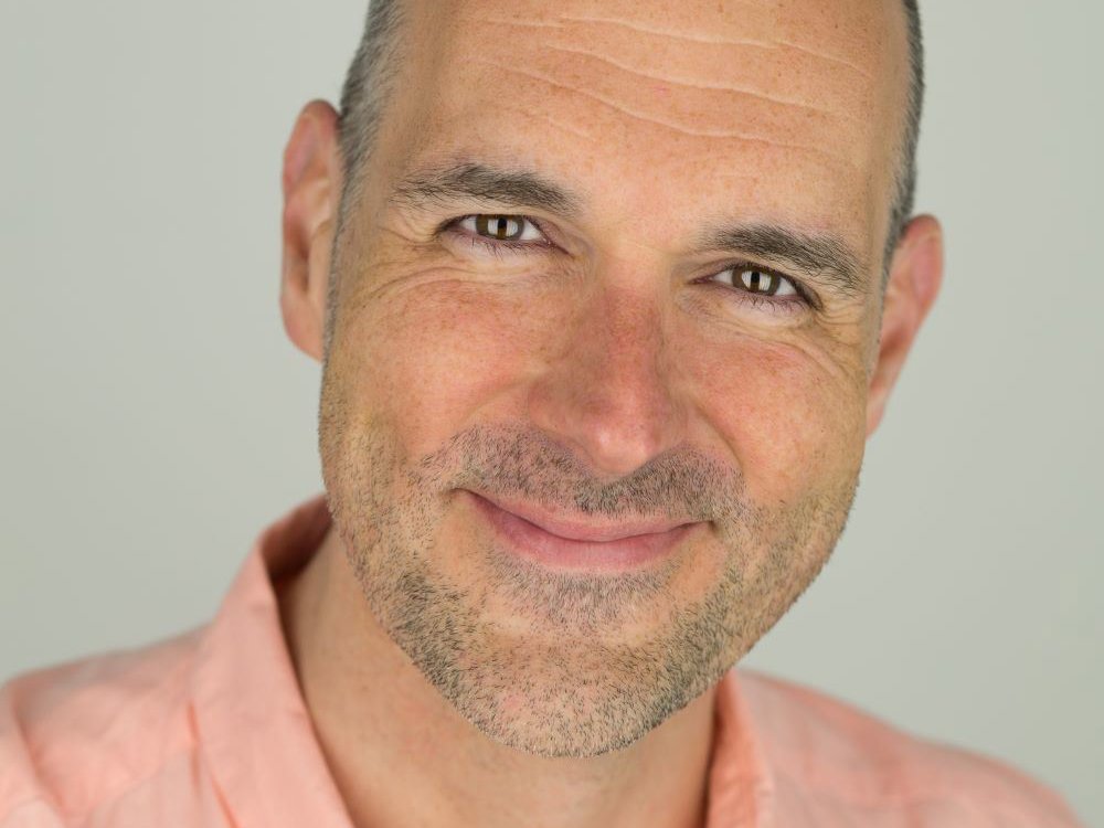 Headshot of James McLean. He is bald with a neatly trimmed beard and is wearing a light peach shirt. James is smiling warmly and looking directly at the camera, giving a friendly and approachable expression. 