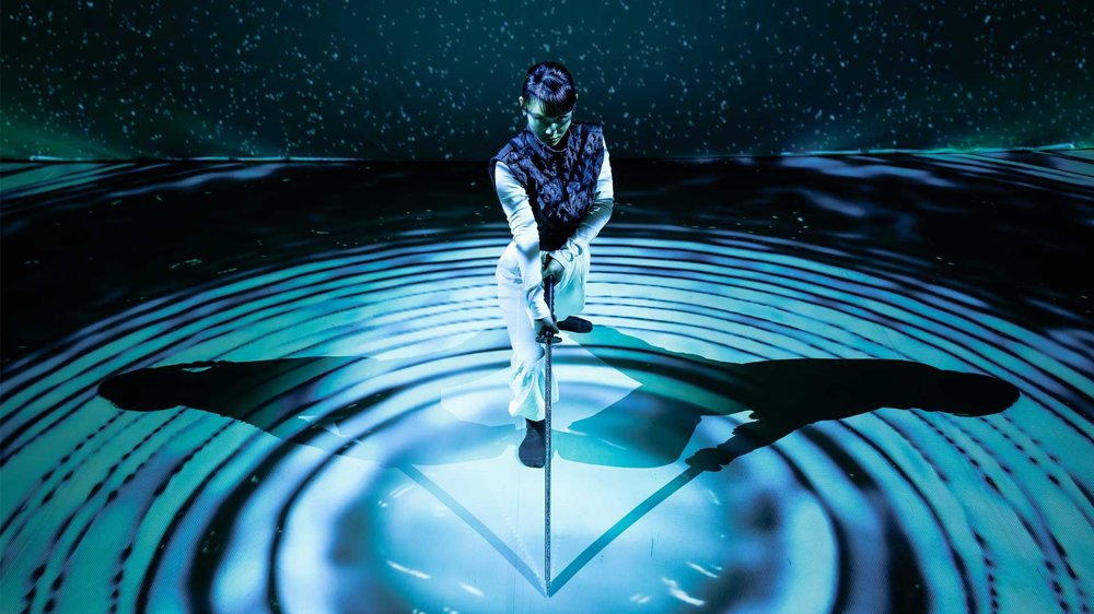 An image of a dancer with a sword amid blue circular light patterns and shadows.