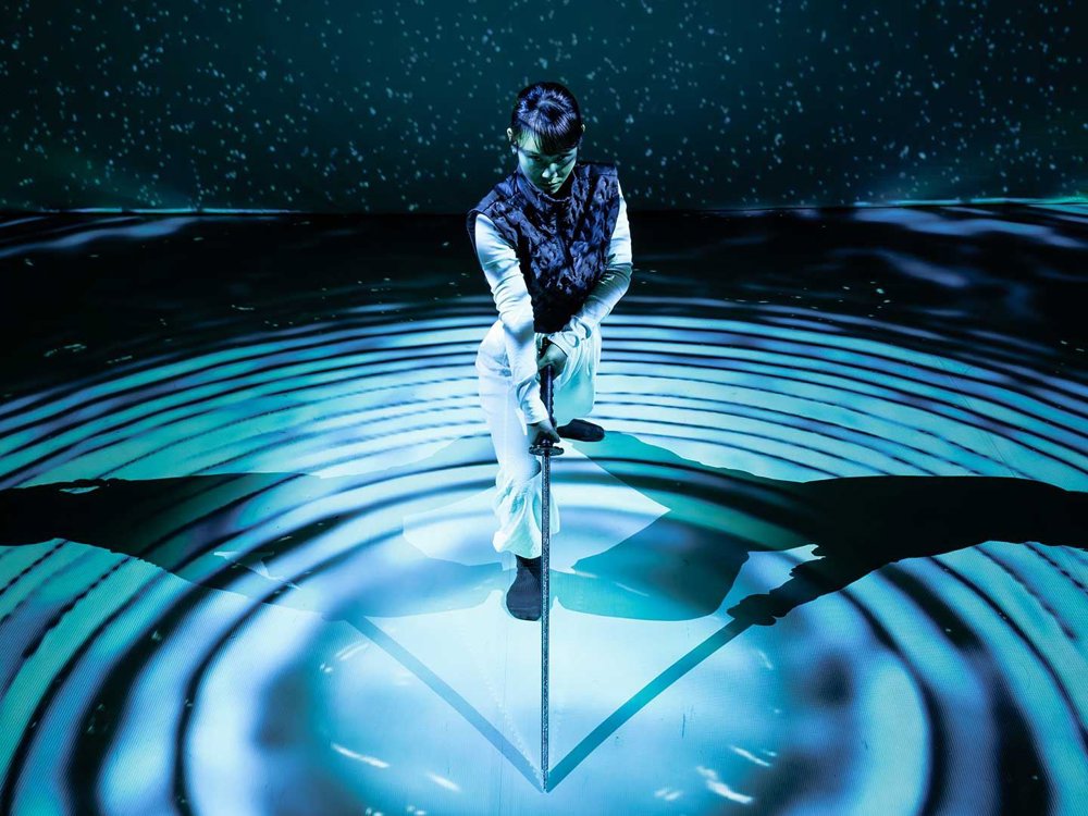 An image of a dancer with a sword amid blue circular light patterns and shadows.