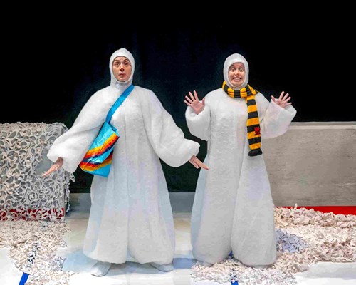 Two actors from Snowmen, each dressed in a fluffy, white onesie. One snowman wears a yellow and green striped scarf.  