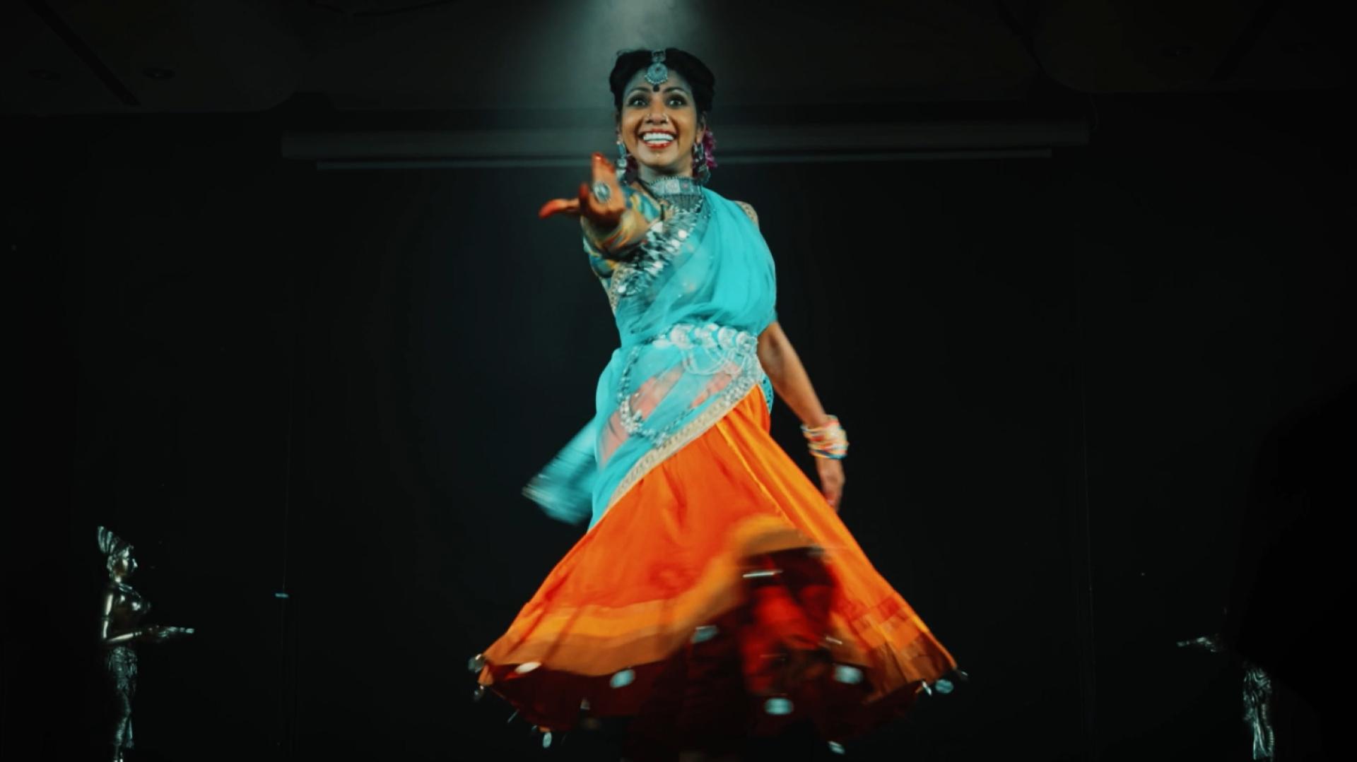 Woman in traditional south asian dress dances wearing a happy inviting face looking towards the camera