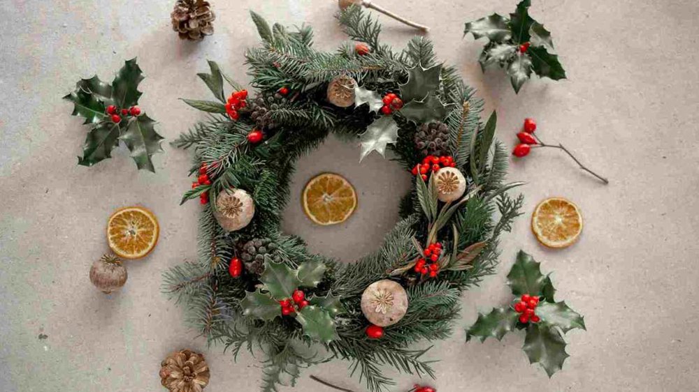 Handmade evergreen Christmas wreath decorated with holly, red berries, pine cones, dried orange slices and natural seed pods.