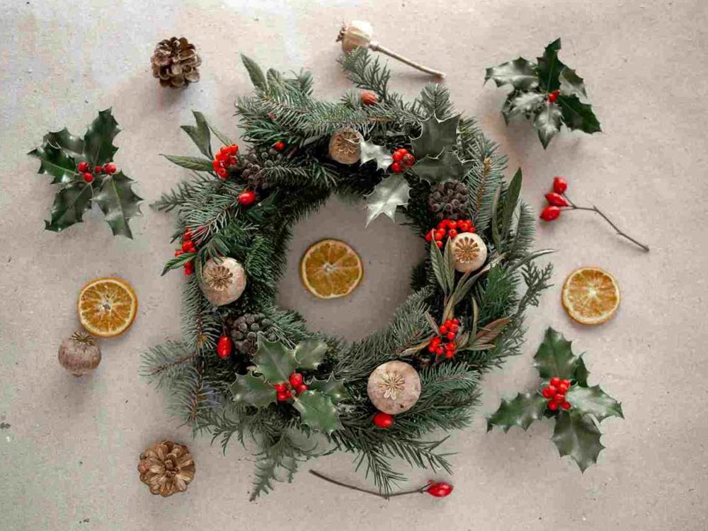 Handmade evergreen Christmas wreath decorated with holly, red berries, pine cones, dried orange slices and natural seed pods.