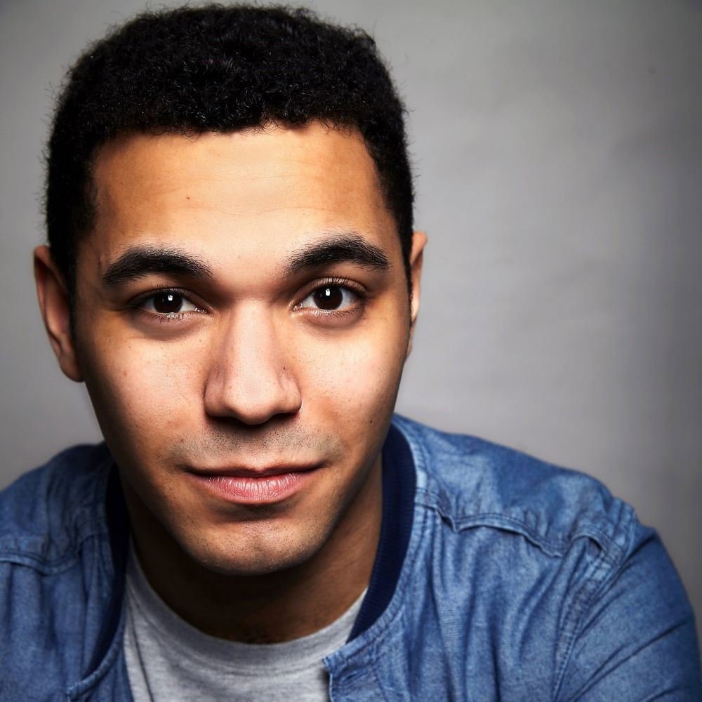 Headshot of Reece Carter. He has short curly hair, wears a denim jacket over a grey t-shirt, and looks directly at the camera with a slight smile.