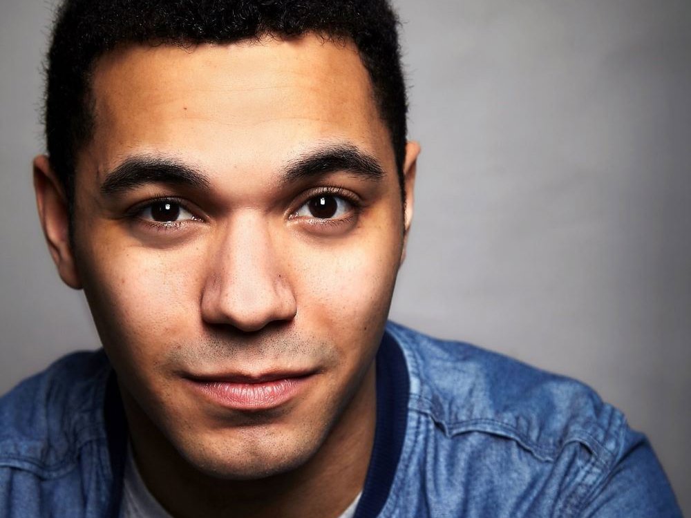 Headshot of Reece Carter. He has short curly hair, wears a denim jacket over a grey t-shirt, and looks directly at the camera with a slight smile.