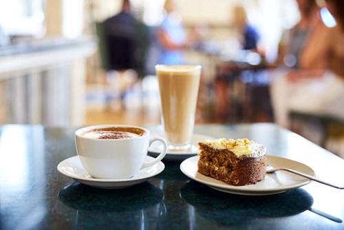 On a table are a cup of coffee, a latte and a slice of cake.