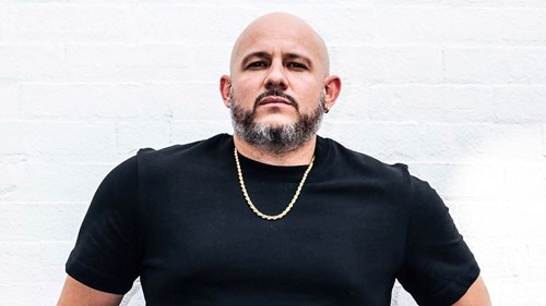 Comedian White Yardie wearing a black t-shirt with a gold chain around his neck.