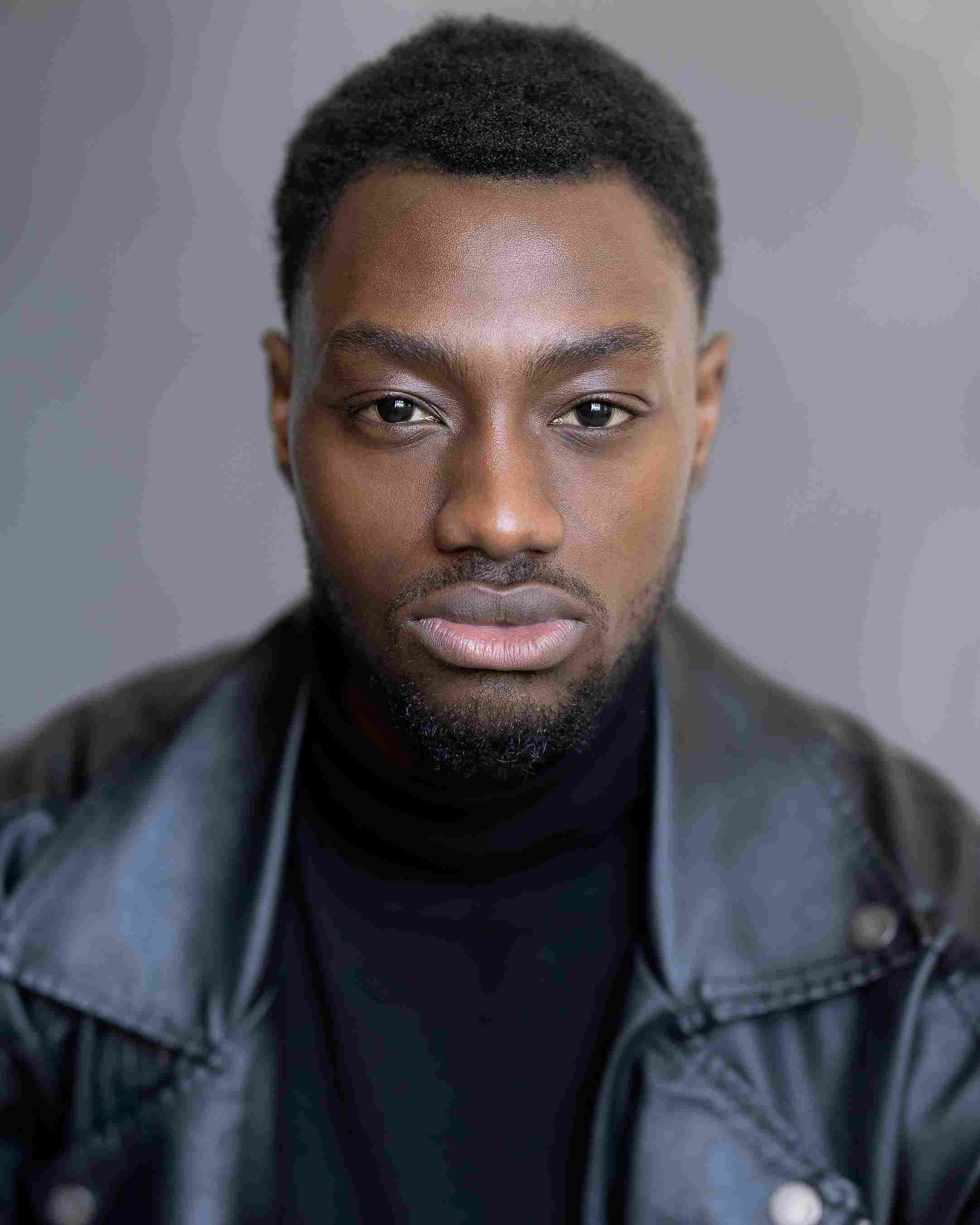 Oluwalonimi (Nimi) Owoyemi: Portrait of a man with short hair and beard, wearing a black turtleneck and leather jacket, looking directly at the camera with a neutral expression.