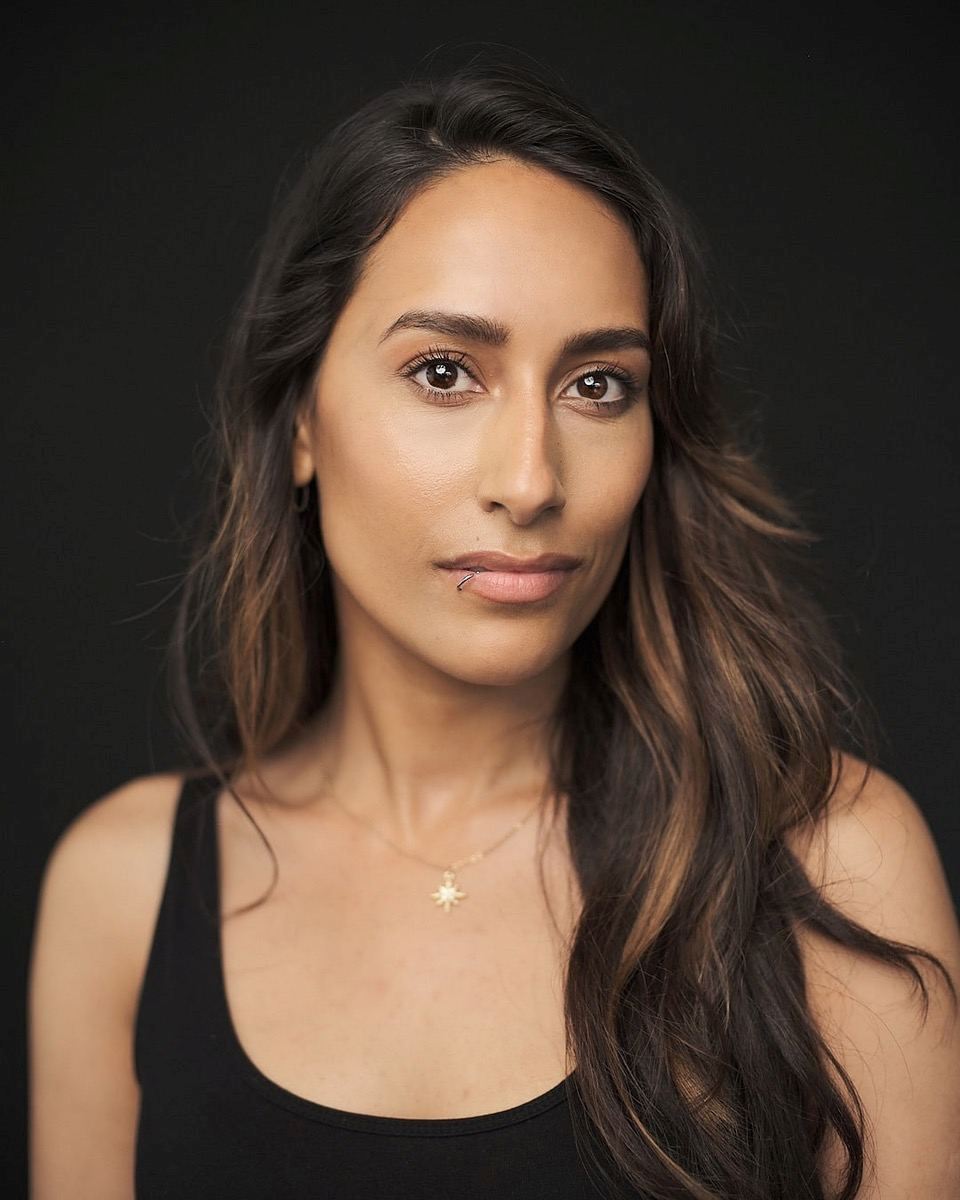 Sonia Wrightson: Woman with long brown hair wearing a black vest top and gold necklace, posing in front of a dark background with a neutral expression.