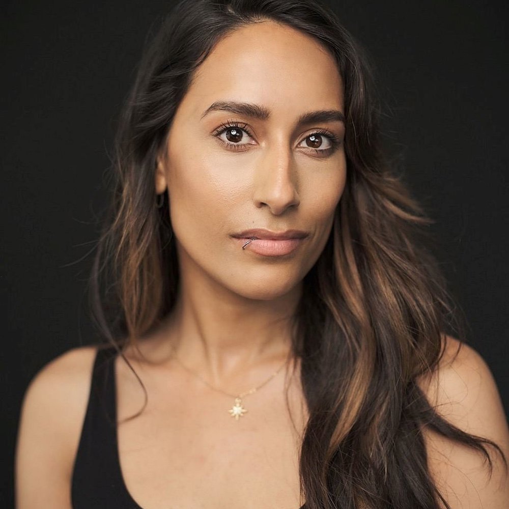 Sonia Wrightson: Woman with long brown hair wearing a black vest top and gold necklace, posing in front of a dark background with a neutral expression.