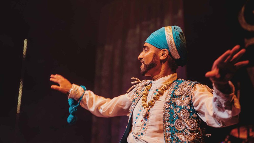 Bhangra specialist Hardeep Sahota is captured mid-movement as he dances wearing a bright blue turban and white and blue Punjabi dress.