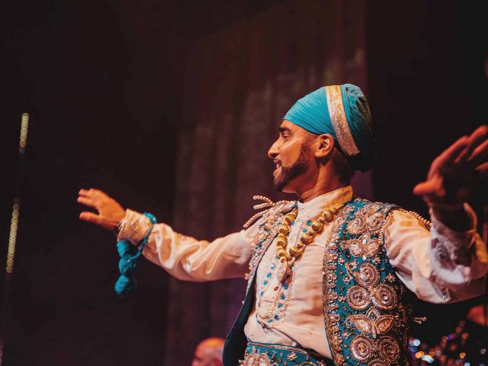 Bhangra specialist Hardeep Sahota is captured mid-movement as he dances wearing a bright blue turban and white and blue Punjabi dress.
