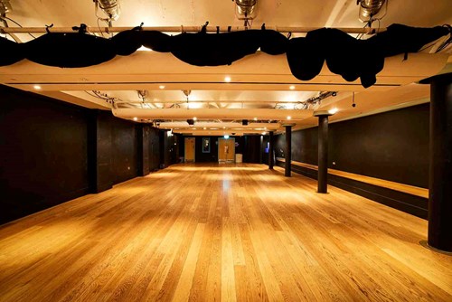 The Lawrence Batley theatre's Cellar Theatre. A large space with wooden floors and painted black walls with a lighting rig on the ceiling. 