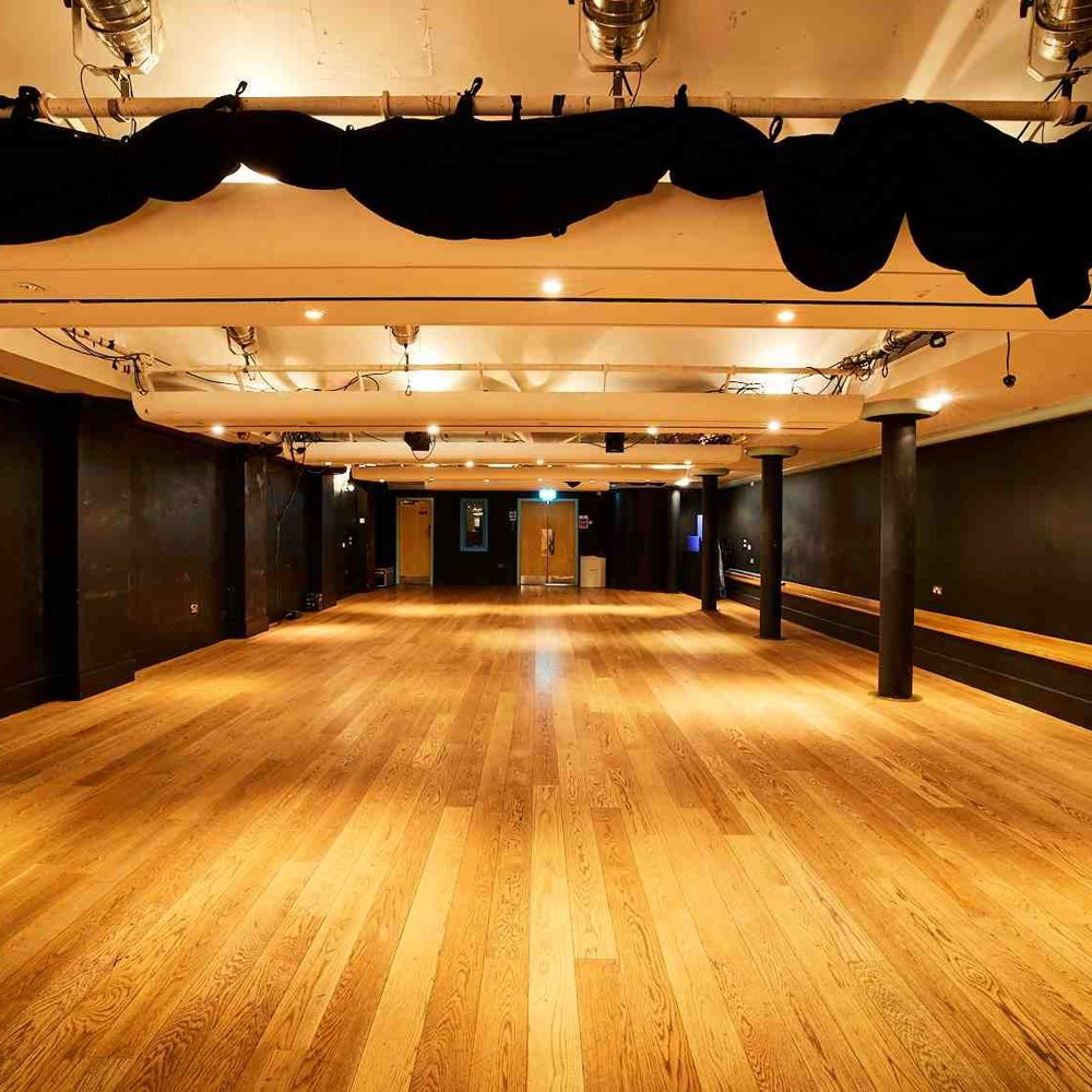 The Lawrence Batley theatre's Cellar Theatre. A large space with wooden floors and painted black walls with a lighting rig on the ceiling. 