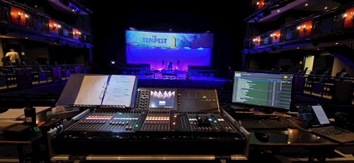 Lighting and sound desk pictured in Lawrence Batley Theatre's Main House. The desk is black with lots of dials and different coloured lights,. there is a computer screen and folder filled with paper next to the desk. 