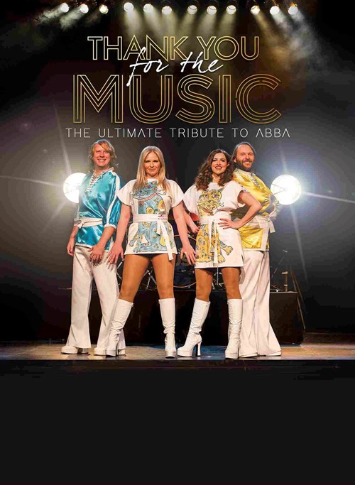Four people stand at the edge of the stage in front of the a drumkit. They all wear big, white boots along with white, flared trousers or white dresses. Their clothing is either patterned with blue or gold designs. 