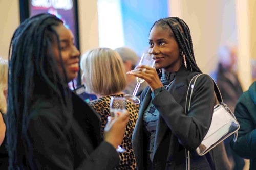 Guests enjoy drinks in the foyer at Lawrence Batley Theatre. One woman smiles while holding a glass, and another sips from a champagne flute, surrounded by a lively crowd.