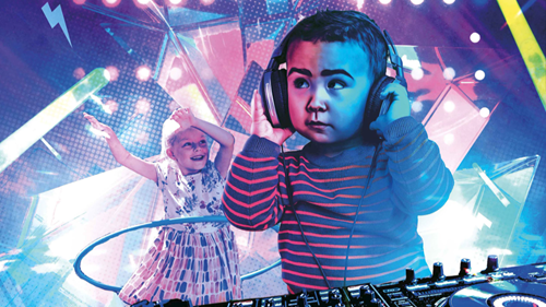 A young child wearing large headphones and a striped jumper stands in front of DJ equipment, appearing focused and engaged in the music. In the background, another child with blonde hair and a floral dress dances energetically with a hula hoop. The scene is set against a vibrant, colourful background with dynamic lighting and geometric shapes, creating a lively, party-like atmosphere.