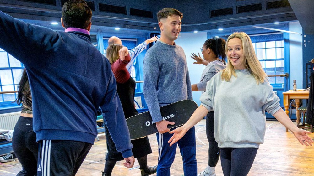 Actors in casual clothes moving around a blue room, with wooden floors at Lawrence Batley Theatre