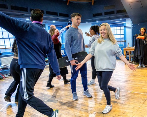 Actors in casual clothes moving around a blue room, with wooden floors at Lawrence Batley Theatre