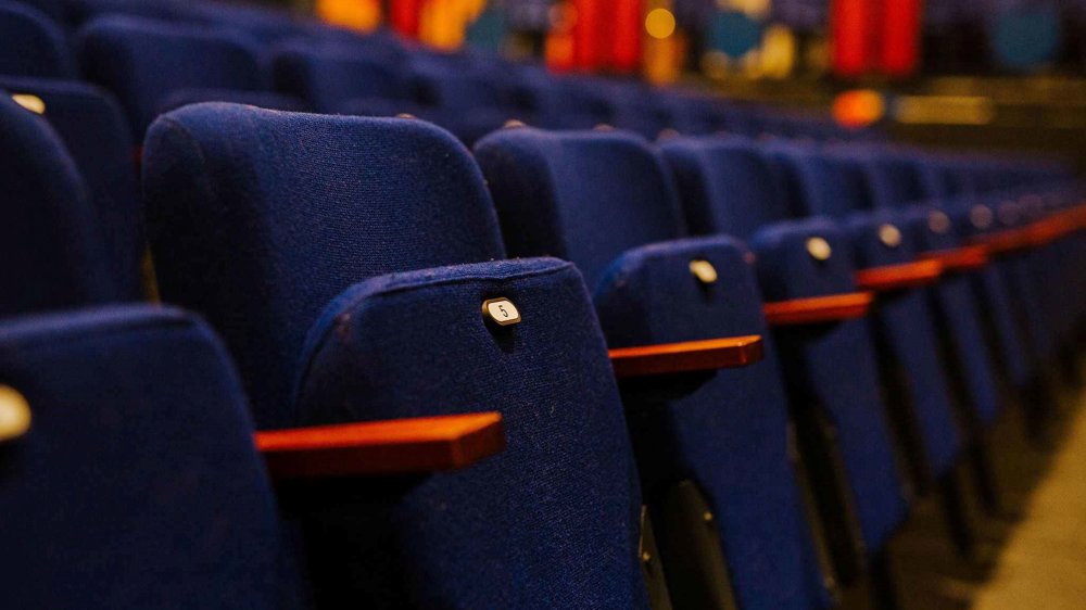 A row of dark blue flip-up seats with wooden armrests. 