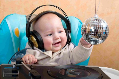 Baby in a highchair wearing headphones that are too big and playing with a tiny disco ball. 