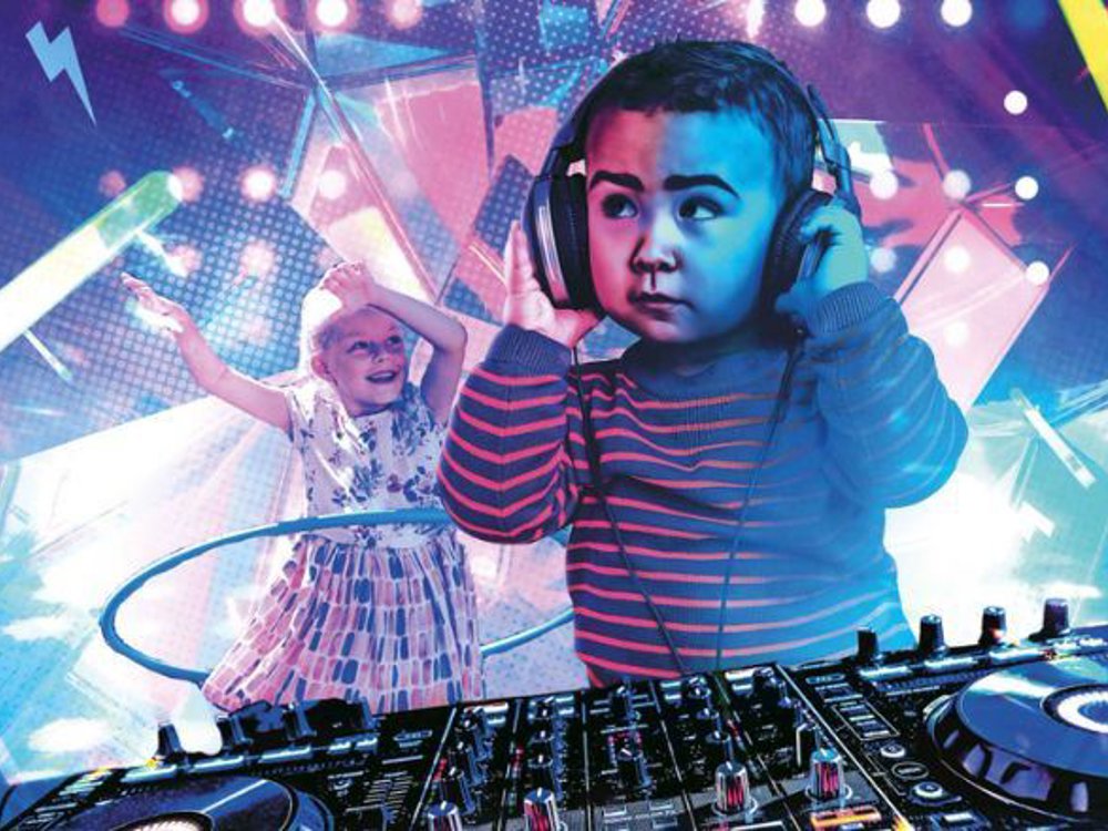 The image features a playful scene of young children in a disco-like environment. In the foreground, a toddler is wearing oversized headphones, standing at a professional DJ deck, as if they are mixing music. The child, dressed in a striped sweater, looks focused and serious while interacting with the equipment. In the background, another child is joyfully dancing, wearing a patterned dress, with arms raised and a hula hoop around their waist. 