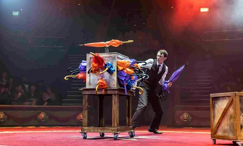 Michael Jordan, performer from High Jinx, pulls an umbrella from a box crammed with colourful umbrellas. 