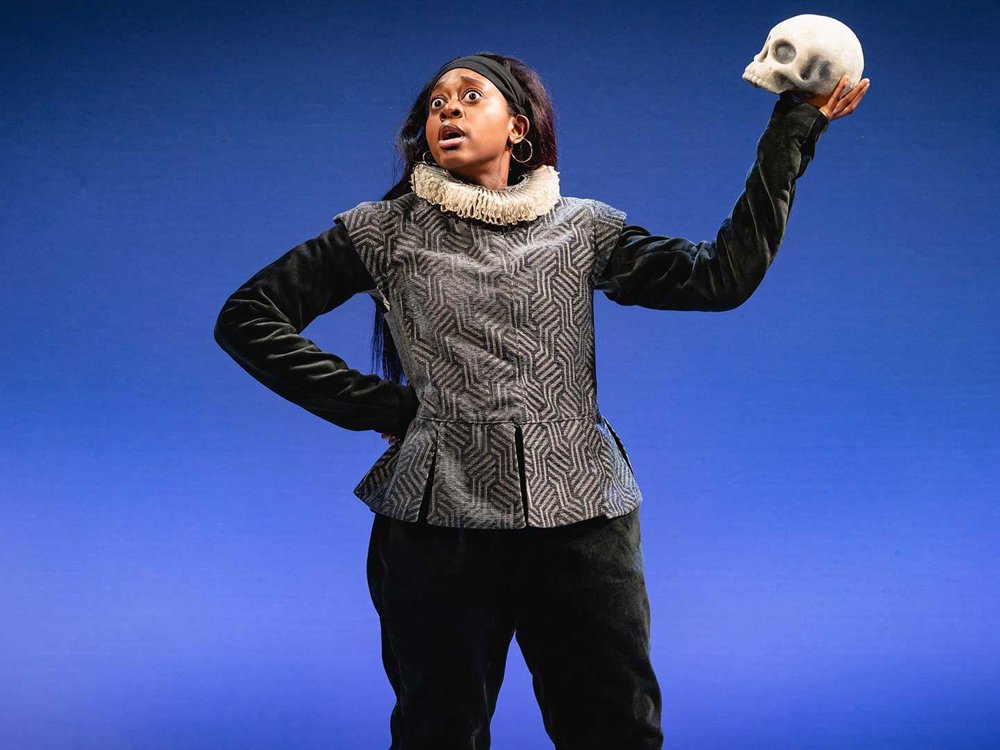 An image of a stage actor dressed in Renaissance-style clothing holds a skull up dramatically against a blue background, evoking a scene from Shakespeare.