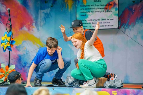 Three children on stage outside Lawrence Batley Theatre. There is a colourful backdrop and the children are crouching as if they may have just finished a dance.
