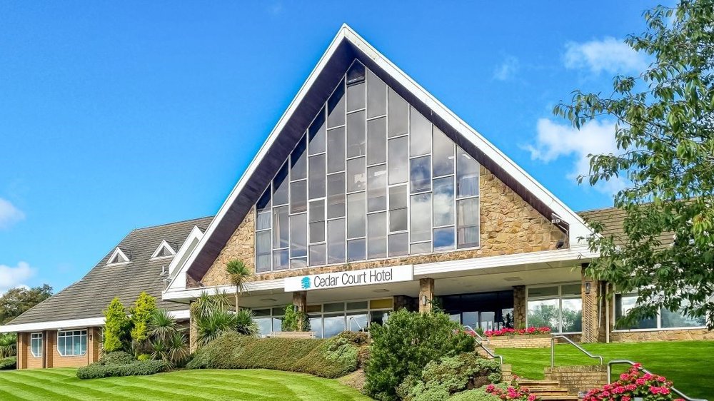 Picture of the front of Cedar Court Hotel Huddersfield, with a large pitch roof and big windows on a sunny day