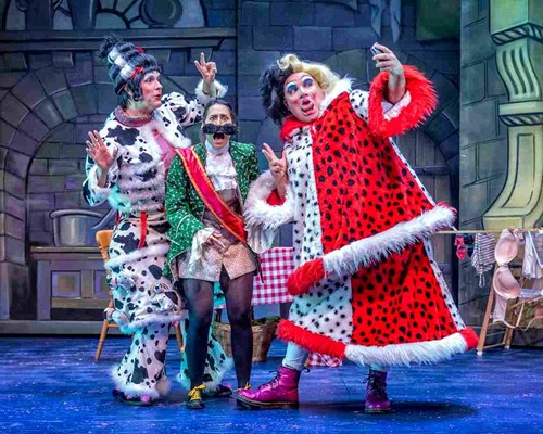 The stepsisters wear outrageous, black and white spotted costumes and colourful wigs. They pose taking a selfie with Dandini, who looks in pain as one of the stepsisters is stood on her foot. 