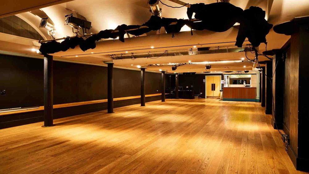 The Lawrence Batley theatre's Cellar Theatre. A large space with wooden floors and painted black walls with a lighting rig on the ceiling. 