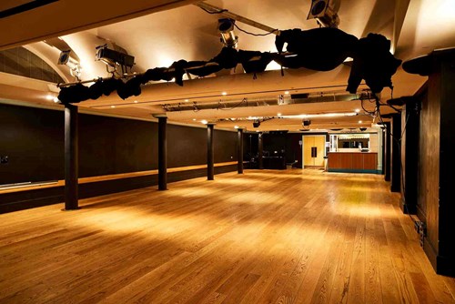 The Lawrence Batley theatre's Cellar Theatre. A large space with wooden floors and painted black walls with a lighting rig on the ceiling.