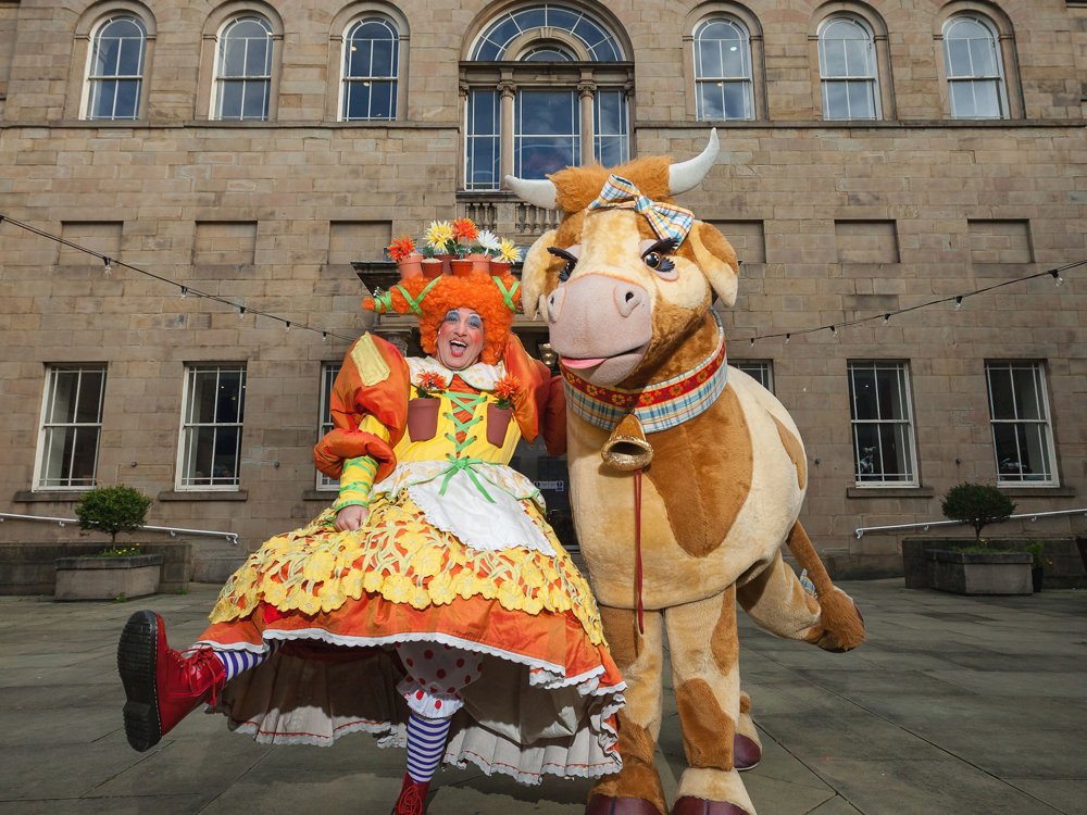 A photograph of a pantomime dame and cow in front of the theatre.