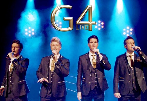 The four members of G4 are dressed in matching black suits with white shirts and gold ties. Each member holds a microphone and is captured singing into it. 