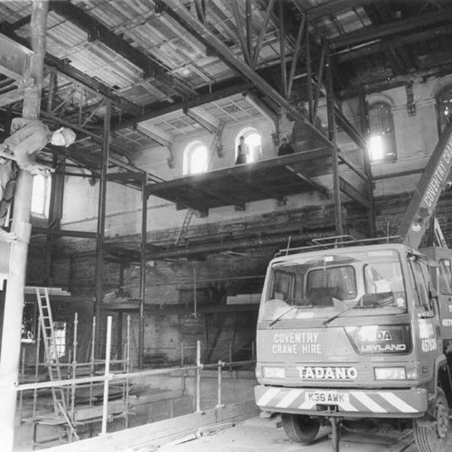 A photograph of the main auditorium during construction in the early 1990s. There is a large crane and a number of builders wearing hard hats around the construction site.