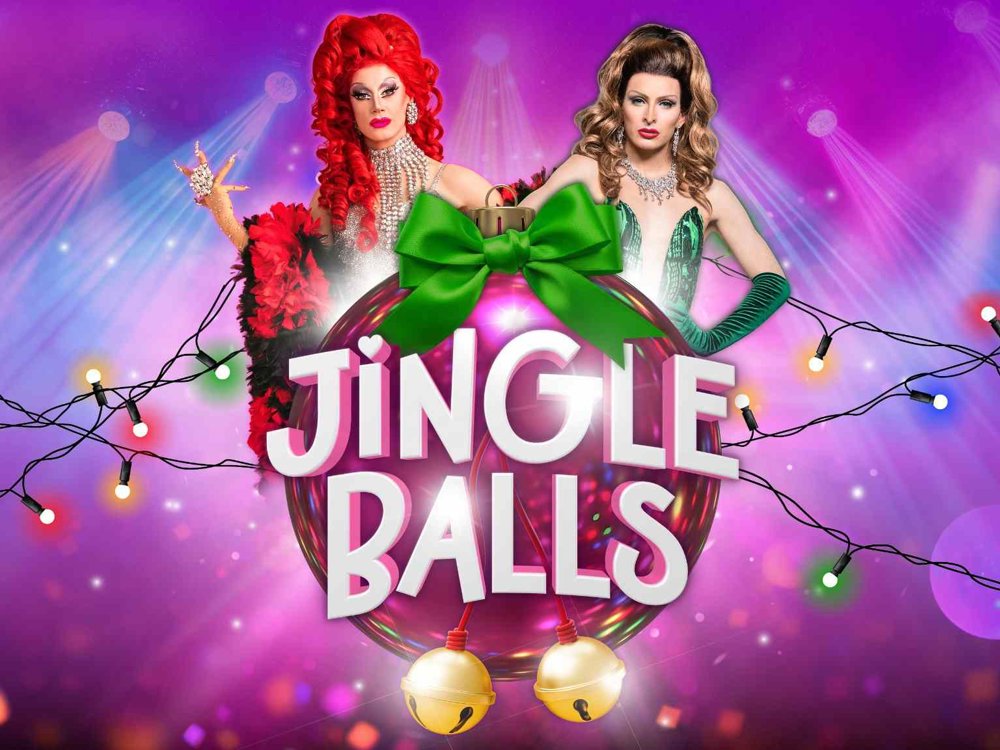 Colourful Christmas-themed promotional artwork for Jingle Balls, featuring two glamorous drag performers, one with bright red hair and one with brunette hair, posed behind a giant pink bauble tied with a green bow. The title “Jingle Balls” appears prominently in large white lettering, surrounded by festive string lights and golden bells against a vibrant pink and purple background.