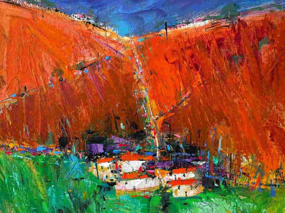A vivid abstract landscape painting by Neville Fleetwood, featuring a striking contrast between bright orange hills and a deep blue sky. At the foot of the hills, a cluster of small white buildings with red roofs sits nestled in a lush green foreground. The composition is bold and textured, with expressive brushstrokes and vibrant colour contrasts.