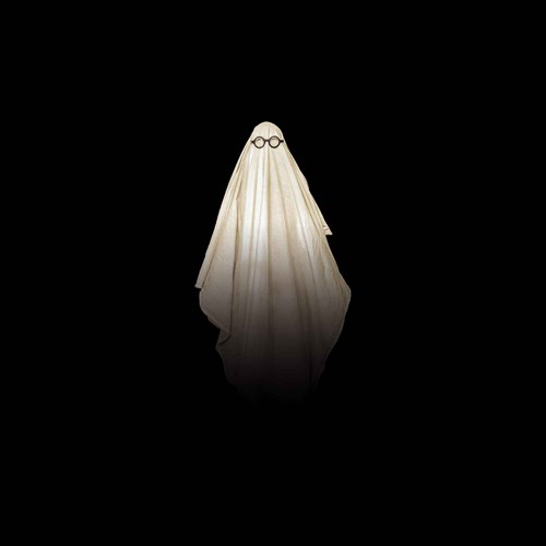 A ghost costume made from a white sheet with round glasses over the eye holes, standing against a completely black background.