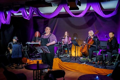 6 musicians performing and playing instruments in front of a purple backdrop