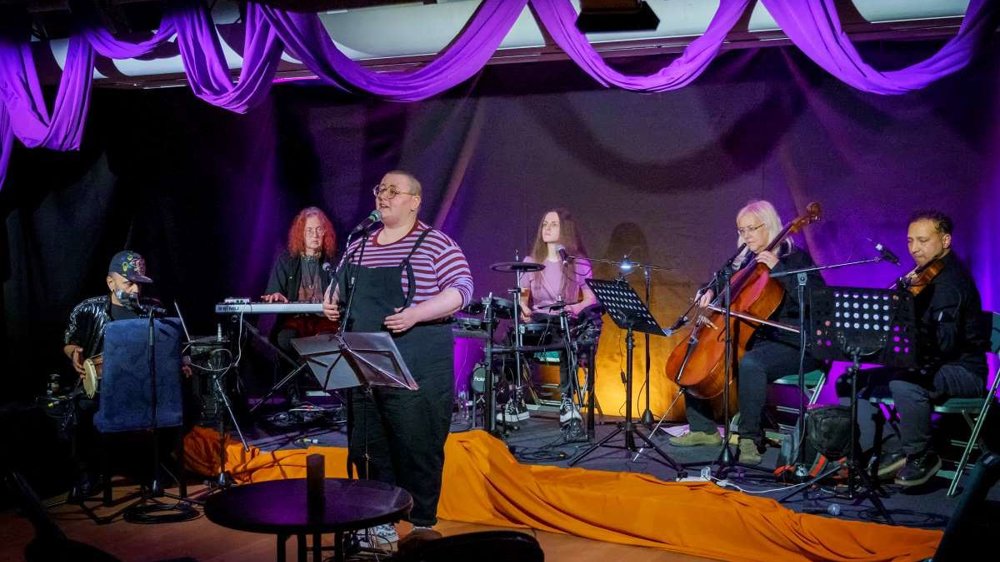 6 musicians performing and playing instruments in front of a purple backdrop
