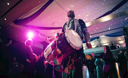 A Dhol player pictured amongst a crowd of dancing people. 