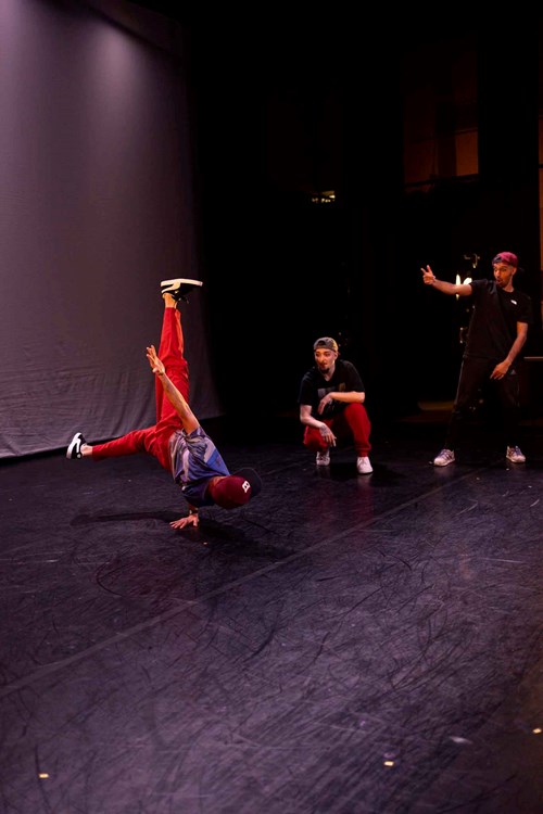Bobak is captured as he breakdances. Two other performers stand behind him. 