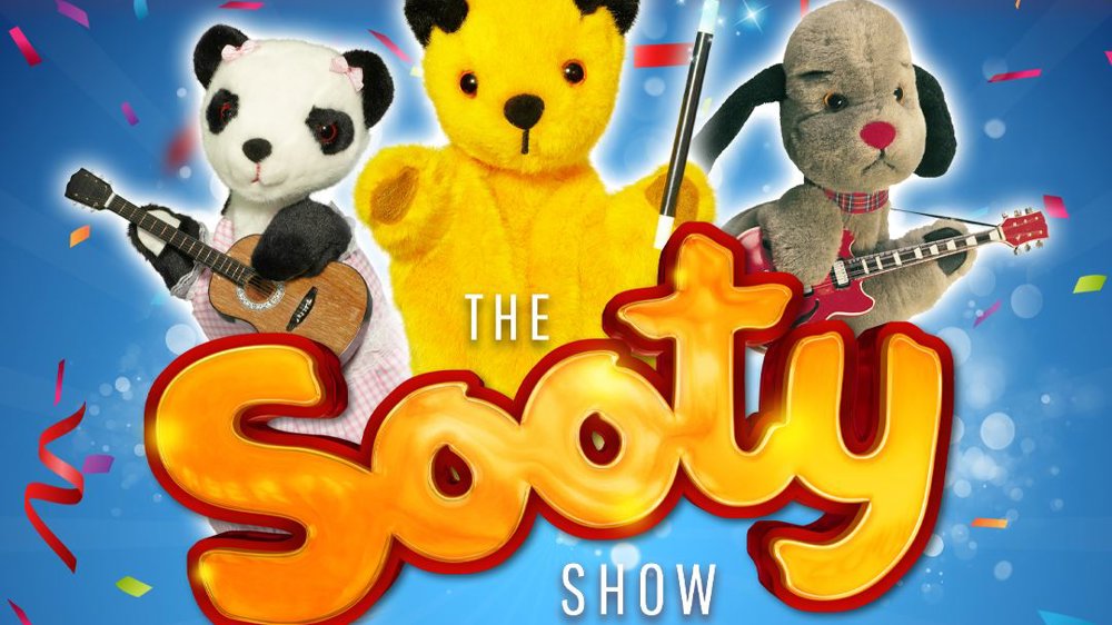 Promotional image for The Sooty Show: The Big Family Laughter Show! featuring puppets Soo, Sooty, and Sweep against a colourful blue and red background with confetti.