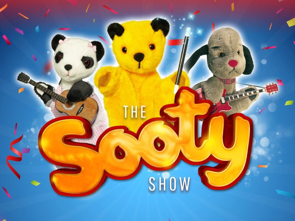 Promotional image for The Sooty Show: The Big Family Laughter Show! featuring puppets Soo, Sooty, and Sweep against a colourful blue and red background with confetti.